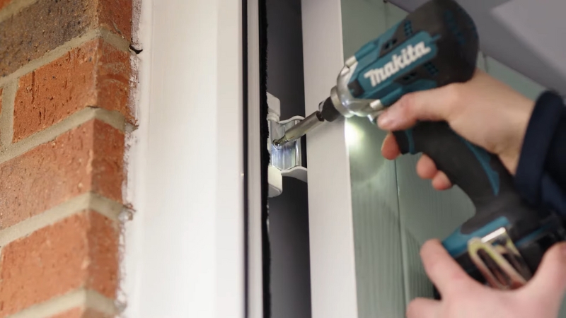 Radnik električnim odvijačem podešava šarku na PVC ili aluminijumskim vratima